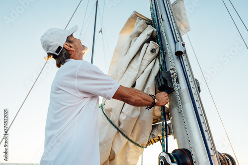 Mature captain looking up while adjusting sail. Senior yachtsman preparing a boat for a vacation trip.