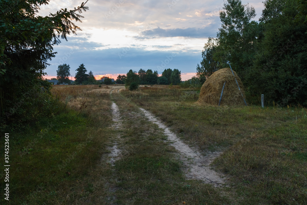 Rural landscape with sunset, road and haystack. Evening
