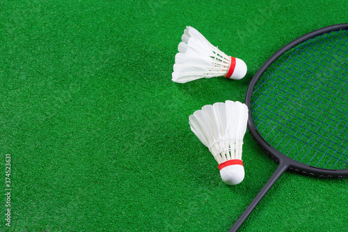 A pair of feathers badminton shuttlecock and racket placed on the green badminton court. Top view, selective focus shot with copy space.