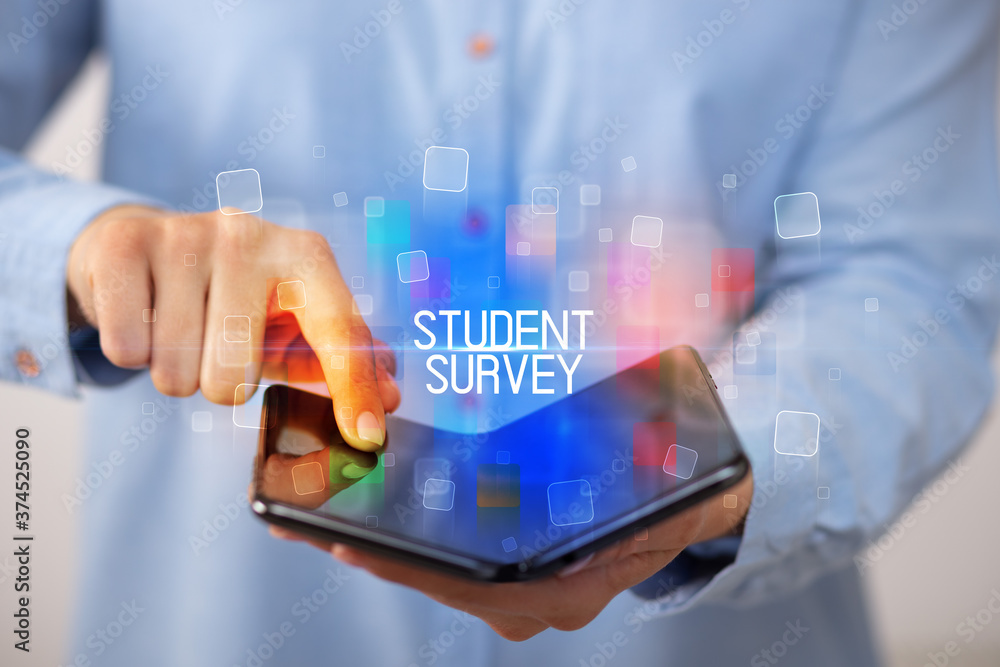 Young man holding a foldable smartphone with STUDENT SURVEY inscription, educational concept Young man holding a foldable smartphone with STUDENT SURVEY inscription, educational concept