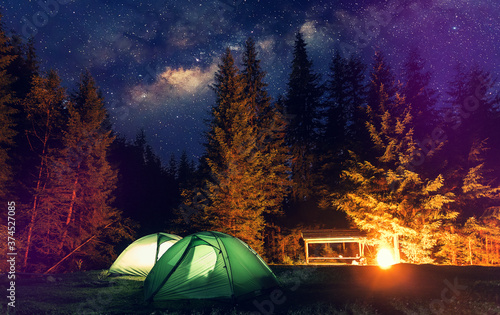 Stunning nature scenery. Tourist camping near forest in night. Illuminated tent and campfire under beautiful night sky Travel recreation, outdoor activity, freedom concept background. instagram filter