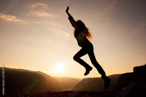 Silhouette einer Frau beim Sprung auf einem Berggipfel