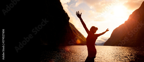 Silhouette einer Frau mit ausgebreiteten Armen bei Sonnenaufgang  an einem See