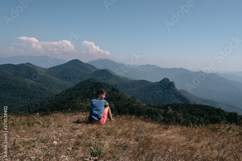 Beautiful mountain and hilly landscape in warm, Sunny weather and the young tourist. A female traveler sits on top of a hill and looks at the surrounding mountains.