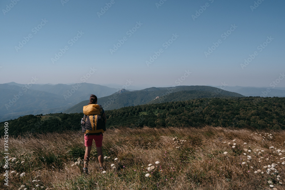 Beautiful landscapes of the national Park and human looking at the mountains, forests and hills. A female traveler stands in the mountains with a large yellow Hiking backpack.