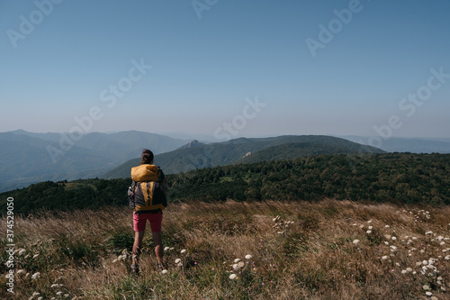 Beautiful landscapes of the national Park and human looking at the mountains, forests and hills. A female traveler stands in the mountains with a large yellow Hiking backpack.
