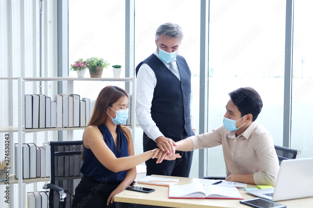 Obraz premium Asian and Caucasian businesspeople teamwork wearing mask preventing for covid 19 virus and joining hands together for successful in jobs and business after meeting and branistom with partner.