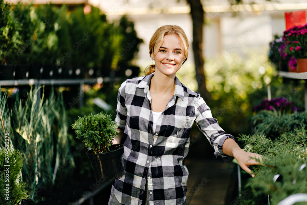 Green-eyed attractive slim girl in stylish shirt with smile poses for portrait in hypermarket in plant department Green-eyed attractive slim girl in stylish shirt with smile poses for portrait in hypermarket in plant department