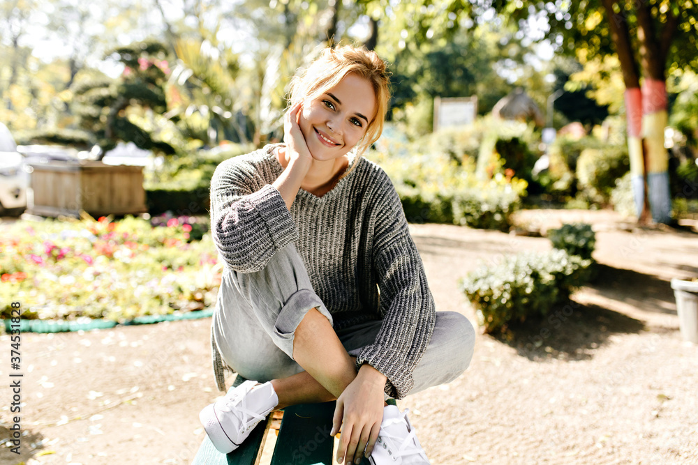 Attractive, charming girl with green eyes sits in cozy place in comfortable position and looks into lens. Full-length photo of model in soft sweater Attractive, charming girl with green eyes sits in cozy place in comfortable position and looks into lens. Full-length photo of model in soft sweater
