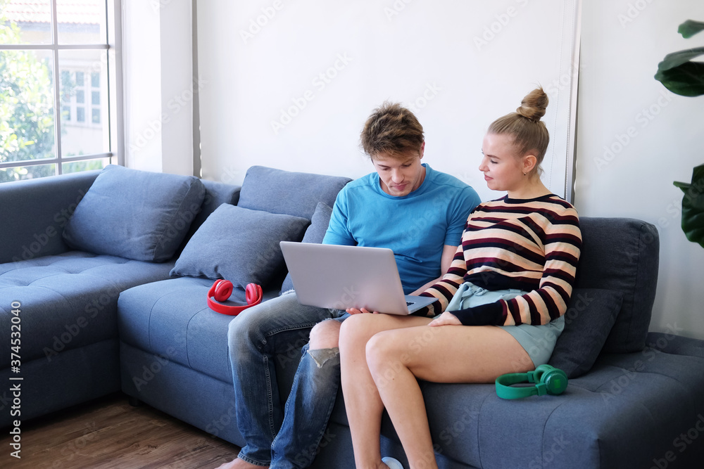 Smiling Young Caucasian couple love relaxing with laptop online for community in social media for shopping in website in living room. Technology for Married family lifestyle on holiday Concept.