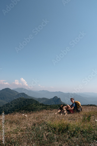 A girl traveler and her German shepherd sit on a hill and look at the mountains around. The dog traveler and its human owner with a backpack walk in the national Park and enjoy nature. © Ekaterina