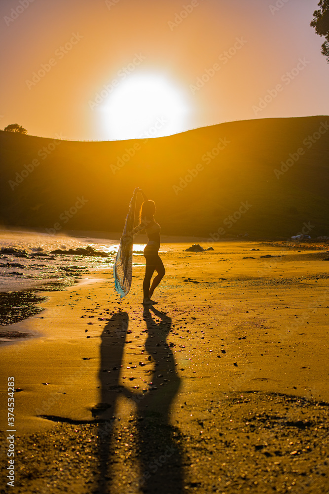young woman doing yoga during sunrise on the beach