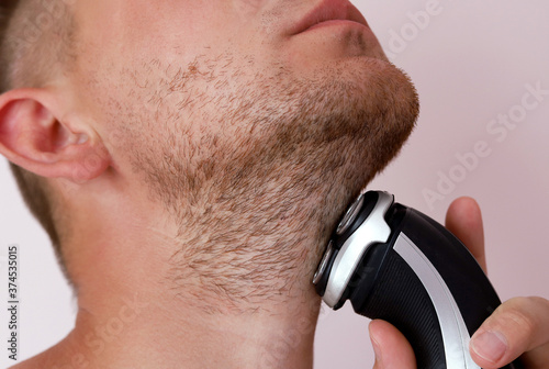 A young Caucasian man shaves the stubble on his face and neck with a shaving machine. Selective focus.A man shaves.