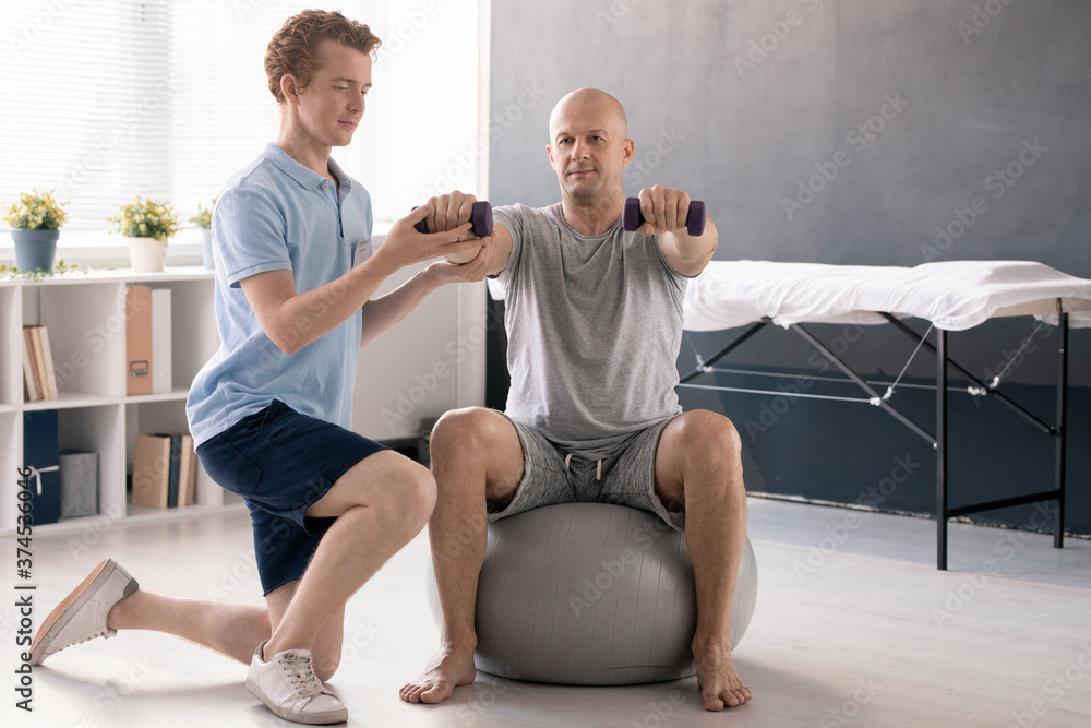 Obraz premium Young physiotherapist in casualwear helping male patient to do exercise