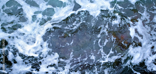 Froth and foam on dark turbulent water, panoramic frame.