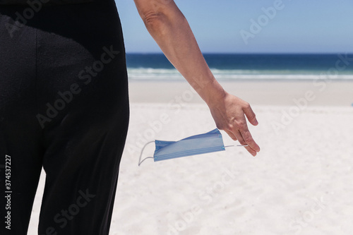 Female hand holding a medical mask with the sea in the background