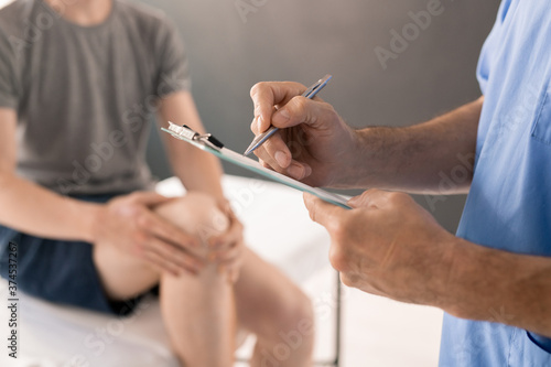 Hands of contemporary male physiotherapist with pen making prescriptions