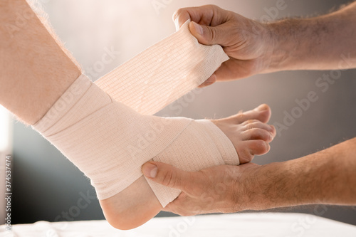 Hands of clinician wrapping foot and leg of patient with flexible bandage © pressmaster