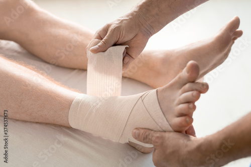 Hands of rehabilitation clinician wrapping foot and ankle of man with bandage © pressmaster