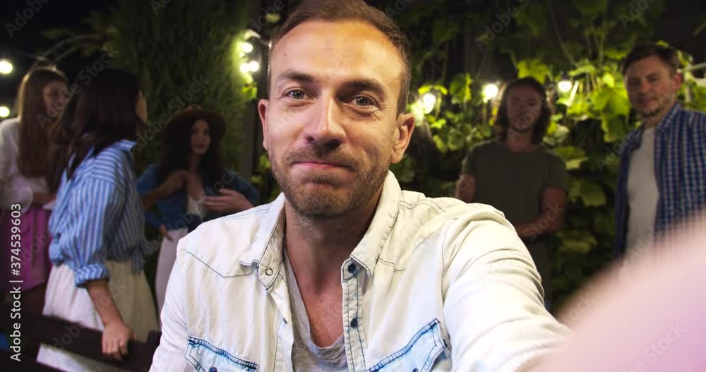 POV of handsome Caucasian man speaking on video outdoor. Beautiful happy African American and Asian girls smiling. Joyful men in good mood. Multi-ethnic friends waving hands at garden party in evening POV of handsome Caucasian man speaking on video outdoor. Beautiful happy African American and Asian girls smiling. Joyful men in good mood. Multi-ethnic friends waving hands at garden party in evening