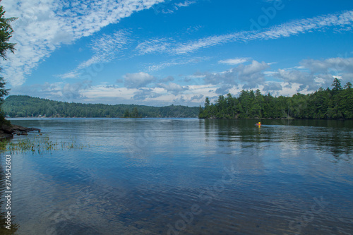 Calm lake surrounded by trees and hills with blue sky and wispy clouds 