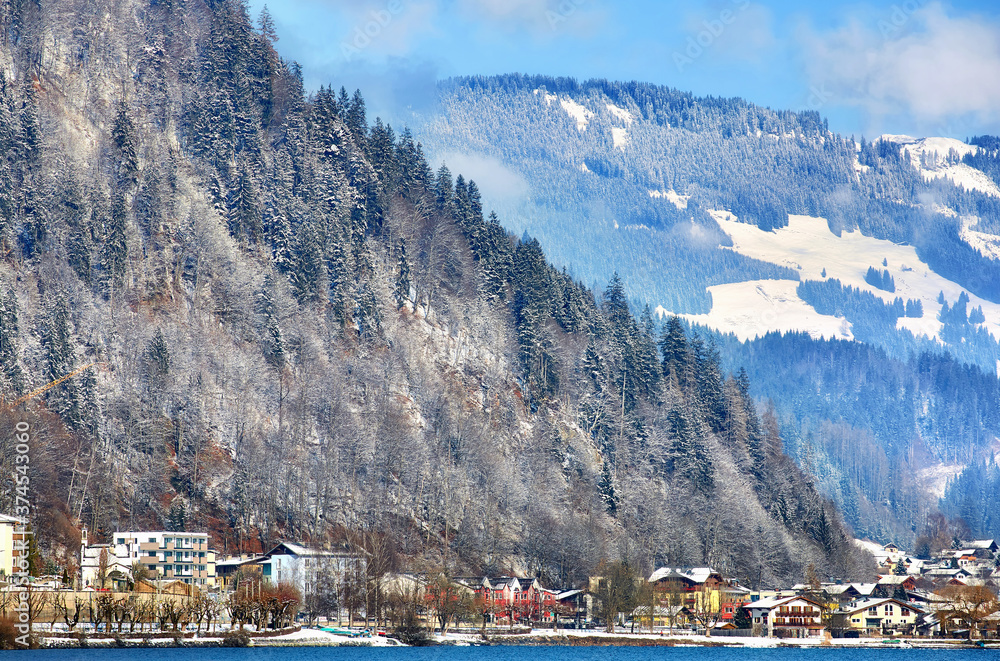 Fototapeta premium Alps with village houses, snow, forest, blue lake and misty clouds