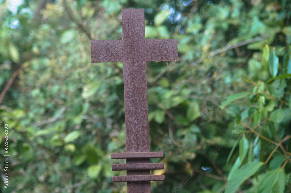 uma cruz enferrujada com uma floresta ao fundo