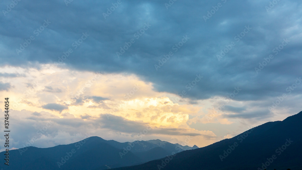 Evening mountain landscape at sunset. Silhouettes of the Pyrenees mountains and the cloudy sky are highlighted by the sun behind the mountains.