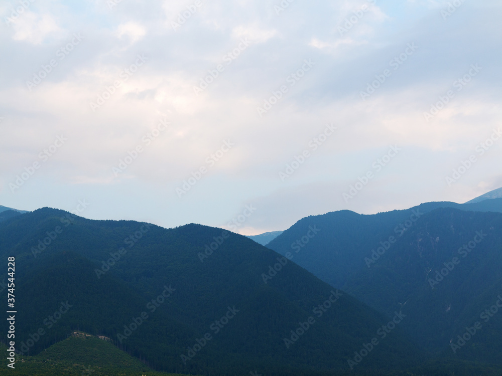 Evening mountain landscape at sunset. Silhouettes of the Pyrenees mountains and the cloudy sky are highlighted by the sun behind the mountains.