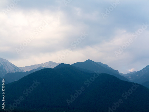 Evening mountain landscape at sunset. Silhouettes of the Pyrenees mountains and the cloudy sky are highlighted by the sun behind the mountains.