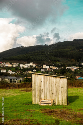Una pequeña cabaña en el campo con una montaña y casas al fondo.