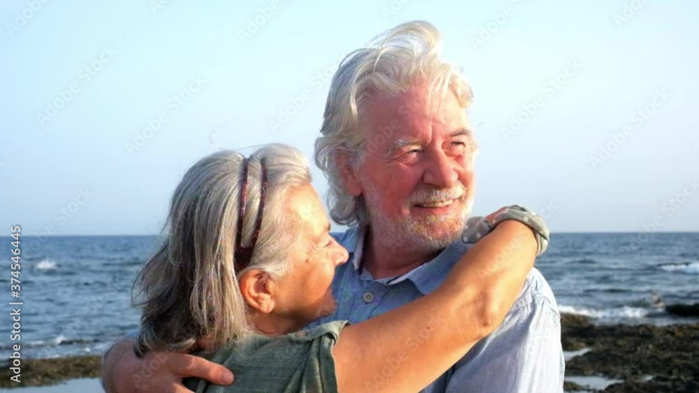 close up and portrait of two happy and active seniors or pensioners having fun and enjoying looking at the camera smiling with the sea at the background - old people outdoors enjoying vacations close up and portrait of two happy and active seniors or pensioners having fun and enjoying looking at the camera smiling with the sea at the background - old people outdoors enjoying vacations