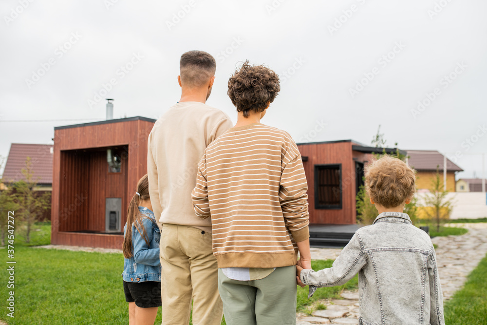 Rear view of family standing on green lawn outdoors in front of new house