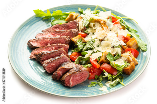 Medium-rare steak and tomato, arugula and parmesan salad on a blue plate