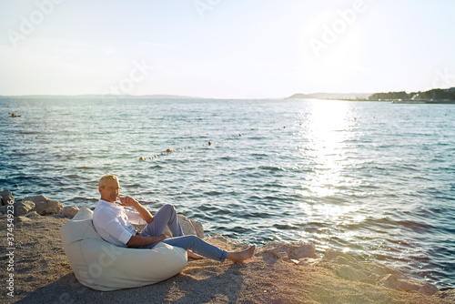 Senior businessman sitting on deck chair on the beach during sunset