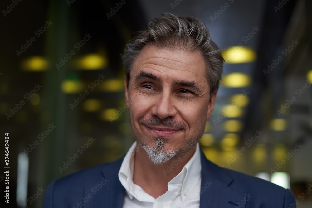 Naklejka premium Portrait of happy mature man smiling and looking at camera. Confident businessman wearing suit, standing in office building hallway.