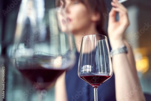 Drinking red wine. Selective focus on wine glass, woman smoking in the background.
