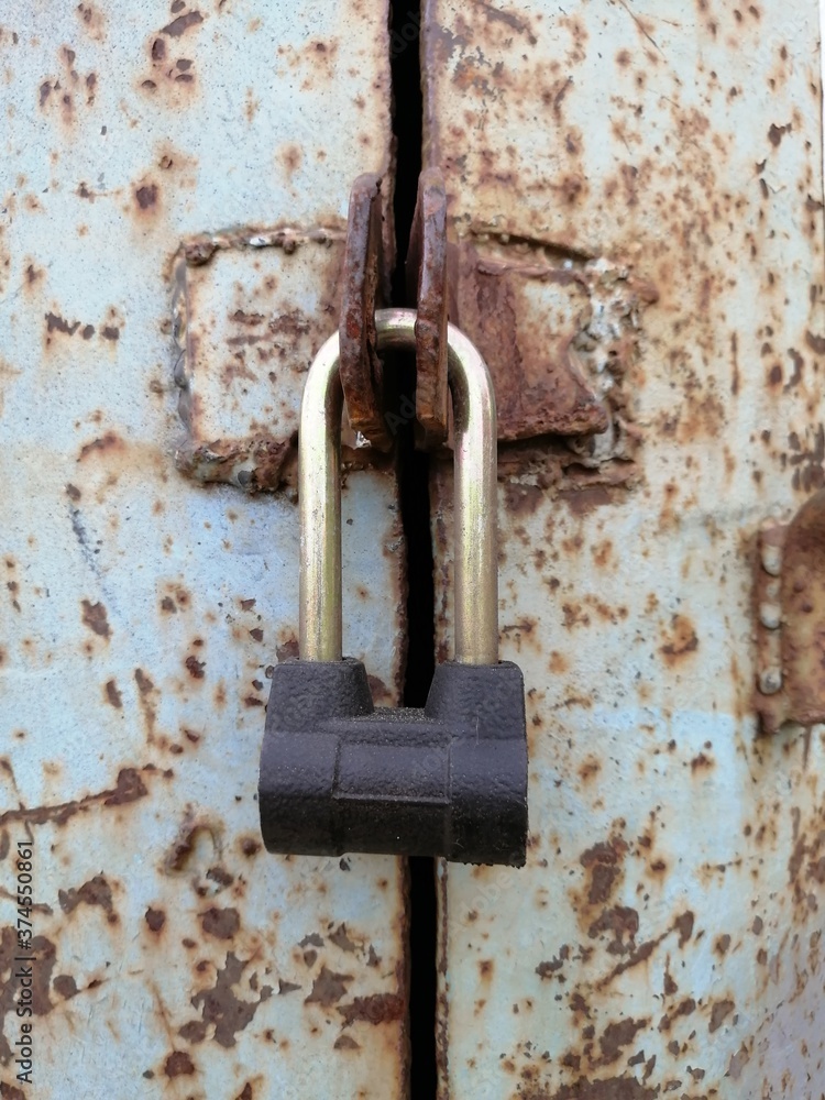 new closed padlock locks the hinges of the old rusty iron door