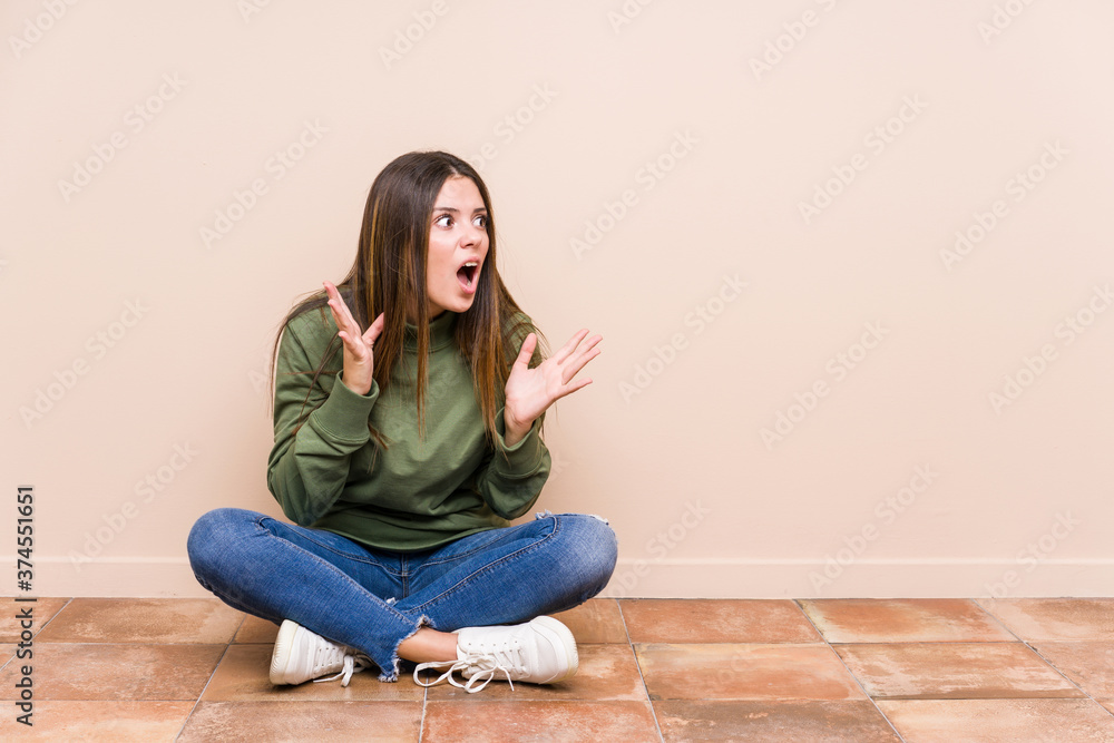 Young caucasian woman sitting on the floor isolated shouts loud, keeps eyes opened and hands tense.