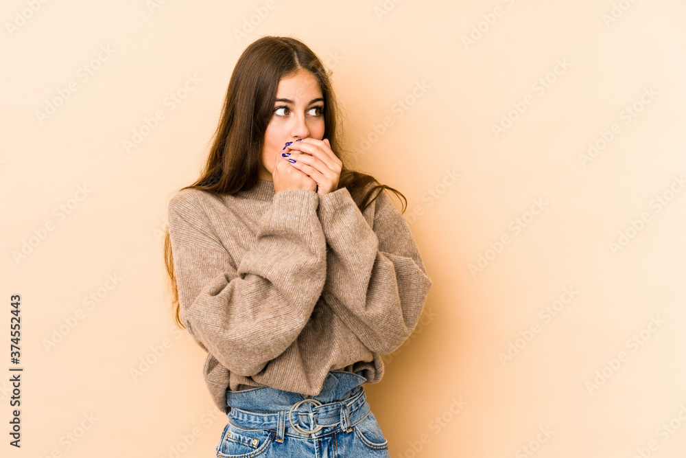 Young caucasian woman isolated en beige background thoughtful looking to a copy space covering mouth with hand. Young caucasian woman isolated en beige background thoughtful looking to a copy space covering mouth with hand.