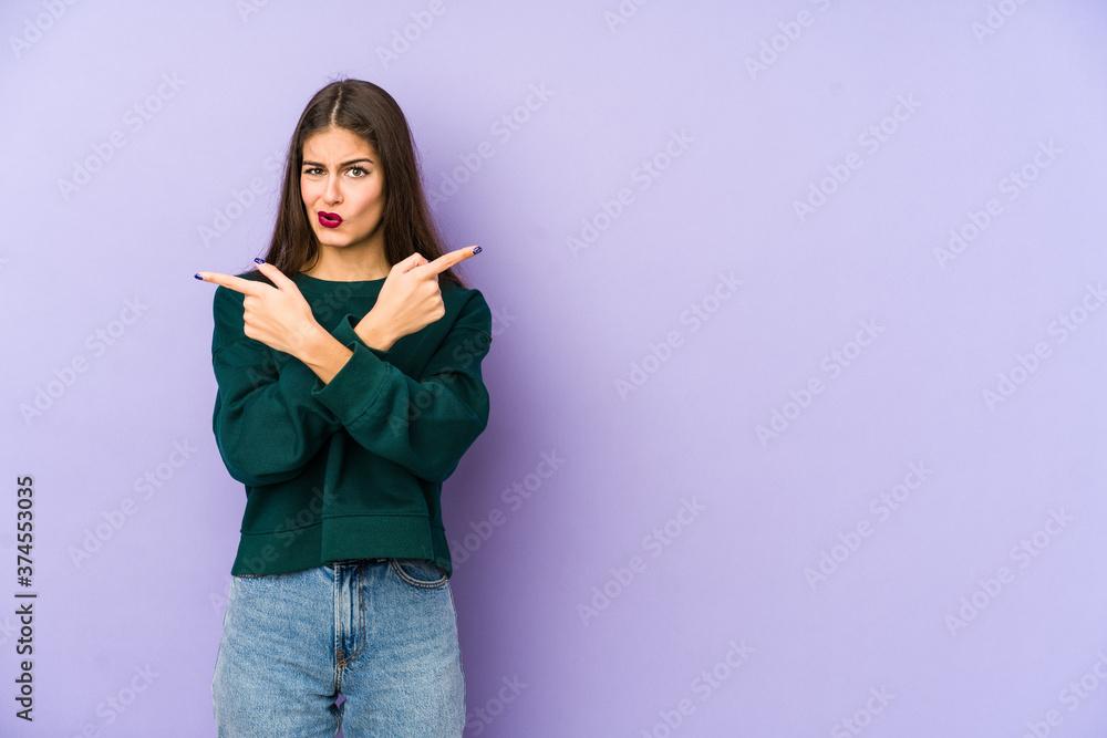 Young caucasian woman isolated on purple background points sideways, is trying to choose between two options. Young caucasian woman isolated on purple background points sideways, is trying to choose between two options.