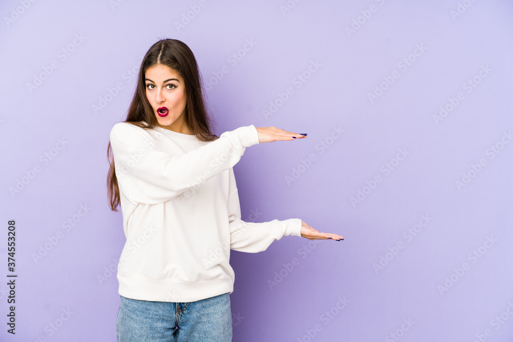 Young caucasian woman isolated on purple background shocked and amazed holding a copy space between hands. Young caucasian woman isolated on purple background shocked and amazed holding a copy space between hands.