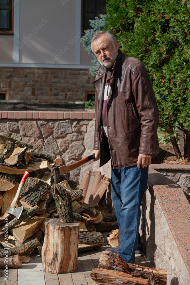 Elderly man in jacket stands in front of pile firewood Elderly man in jacket stands in front of pile firewood