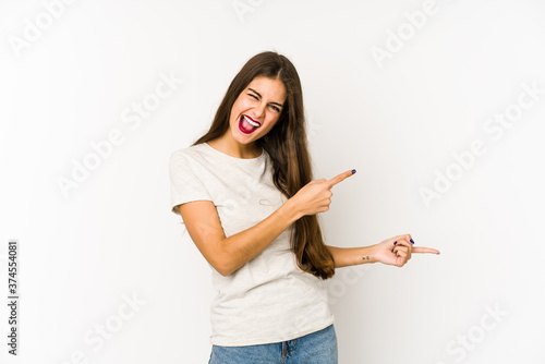 Young caucasian woman isolated on white background pointing with forefingers to a copy space, expressing excitement and desire.