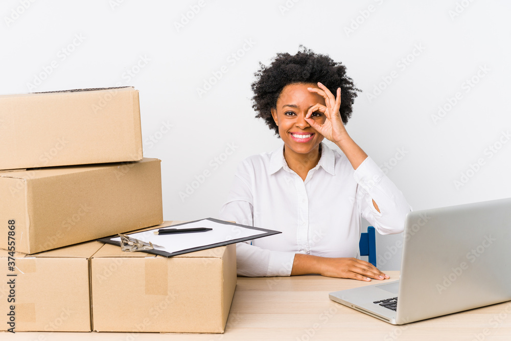 Warehouse manager sitting checking deliveries with laptop excited keeping ok gesture on eye. Warehouse manager sitting checking deliveries with laptop excited keeping ok gesture on eye.