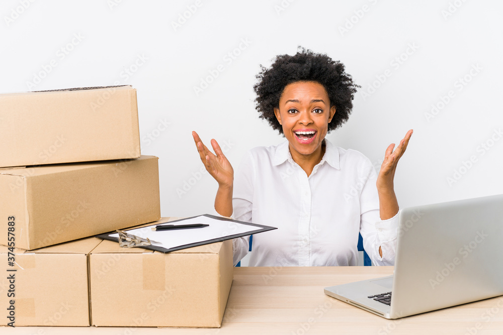 Warehouse manager sitting checking deliveries with laptop receiving a pleasant surprise, excited and raising hands. Warehouse manager sitting checking deliveries with laptop receiving a pleasant surprise, excited and raising hands.