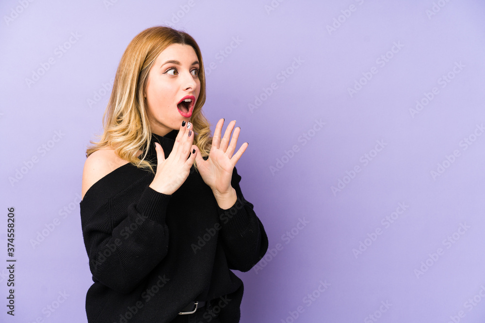 Young blonde woman isolated shouts loud, keeps eyes opened and hands tense. Young blonde woman isolated shouts loud, keeps eyes opened and hands tense.