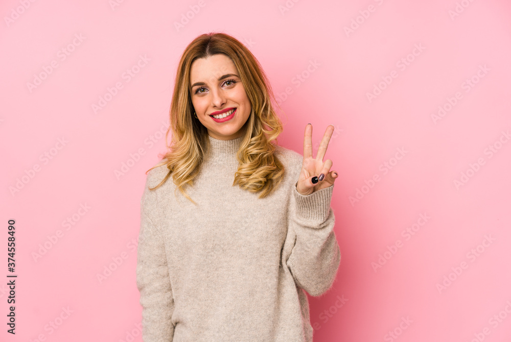 Young blonde cute woman wearing a sweater isolated showing victory sign and smiling broadly. Young blonde cute woman wearing a sweater isolated showing victory sign and smiling broadly.