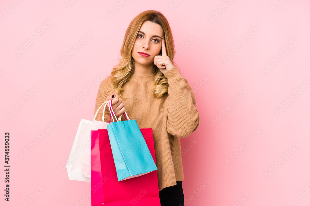 Young blonde woman holding shopping bags isolated pointing temple with finger, thinking, focused on a task. Young blonde woman holding shopping bags isolated pointing temple with finger, thinking, focused on a task.