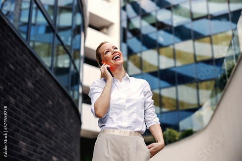 Full length of attractive blond fashionable businesswoman talking on the phone in business center exterior.